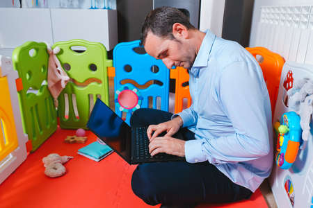 Young businessman has fallen asleep sitting inside his baby's playground at home. Work from home and overtime conceptの写真素材