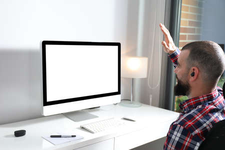 Virtual meeting concept. Young man waving to camera on video call from home office. Computer screen mock up. Copy spaceの写真素材