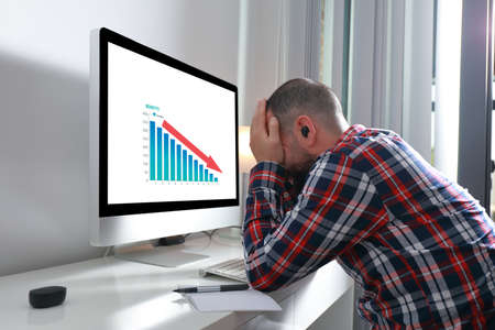 Desperate young man with hands on face in front of computer with bad results on the screen. Crisis, problem, depression conceptの写真素材
