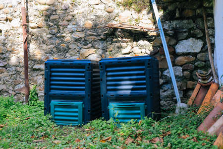 Two plastic compost bins in the garden and stone wall in the backgroundの写真素材