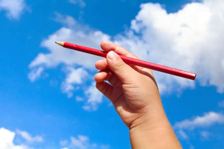 Child holding red pencil on  blue skyの写真素材