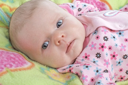 Closeup head and shoulders portrait of a new baby with clothing and blanket in pastel spring colors ...