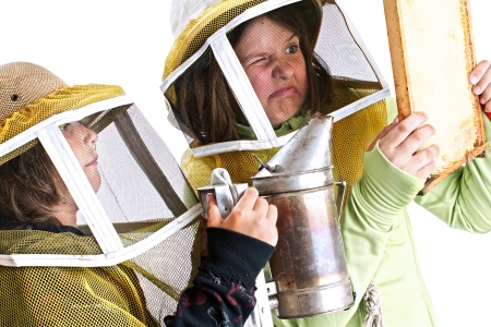 Closeup of an eight year old boy and a twelve year old girl in protective beekeeper hats carefully using a smoker to calm bees in a honey comb  These children are learning beekeeping skills that will protect the environment and encourage locally produced の写真素材