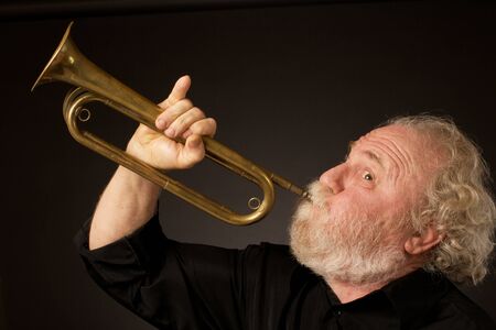 Side view of a bearded senior musician blowing a bugle, held with an expressively raised little...