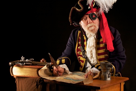Colorful gray bearded pirate captain sits at his desk, drawing a treasure map with a feather quill pen  His musket, a thick leather bound book, and pewter mug are beside him  Dramatic lighting, black background, a horizontal layout, and space for copy の写真素材