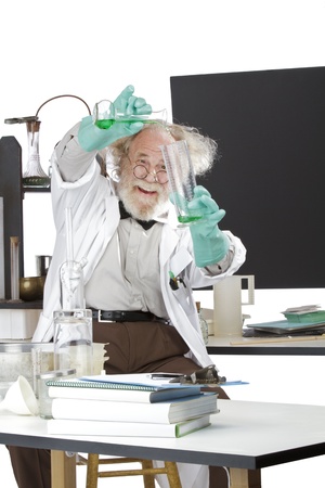 Cheerful mad senior scientist in lab measures green liquid in beaker  Frizzy grey hair, round glasses, lab coat, geek trousers, aqua rubber gloves, blank blackboard, vertical, high key, copy space の写真素材