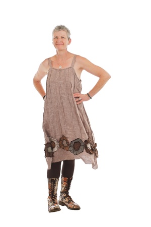 Cheerful friendly older woman stands in flowered boots and brown cotton shift dress. She has short gray hair. Isolated on white background, vertical.の写真素材