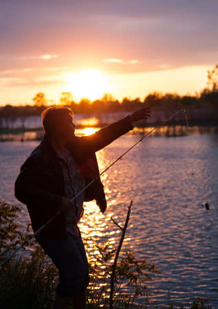 A fisherman with a fishing rod on the river bank の写真素材