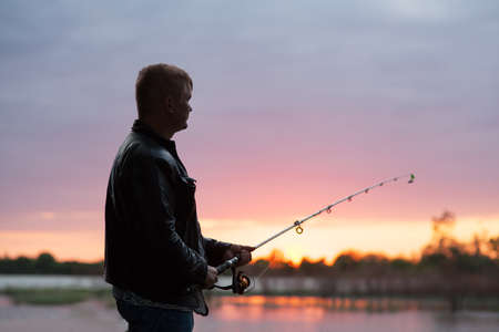 A fisherman with a fishing rod on the river bank の写真素材
