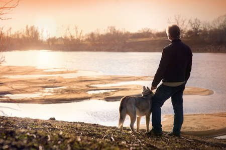 man with a dog on the bank of the river at sunsetの写真素材