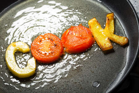 fried vegetables in the form of letters on a frying pan in oilの写真素材