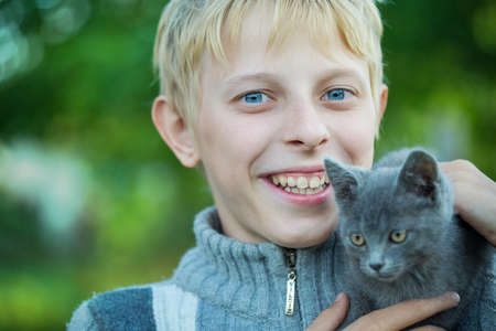 A boy plays with a kitten in the gardenの写真素材