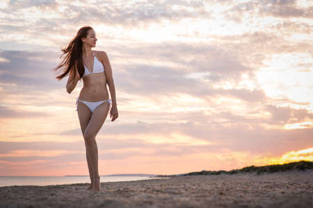 Beautiful girl in a swimsuit on the beach at sunsetの写真素材