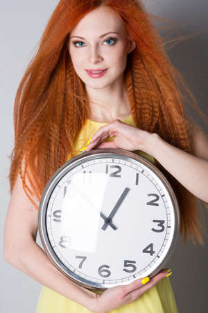 Young woman with red hair holding a big clockの写真素材