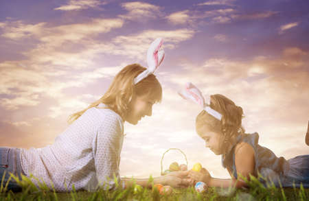Mother and daughter with easter eggs on the grass at sunsetの写真素材