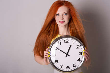 Young woman with red hair holding a big clock