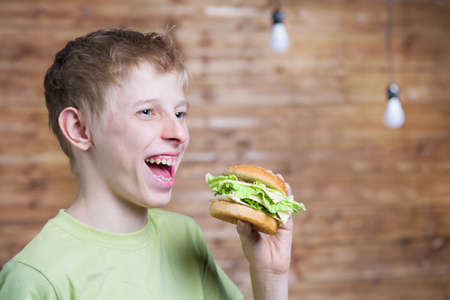 A teenager eating a sandwich with cheese and chopの写真素材