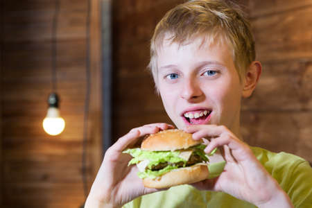 A teenager eating a sandwich with cheese and chopの写真素材