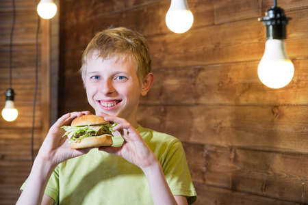 A teenager eating a sandwich with cheese and chopの写真素材