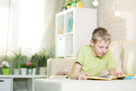 A teenager is reading a book in a room