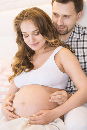 Pregnant wife and husband are sitting on the bed
