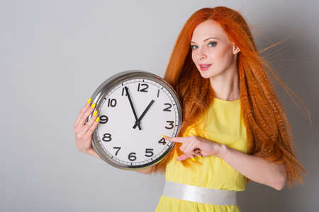Young woman in yellow dress with big clockの写真素材