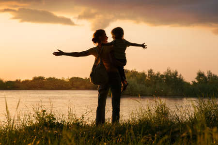 Mom and daughter on the river bank at sunsetの写真素材