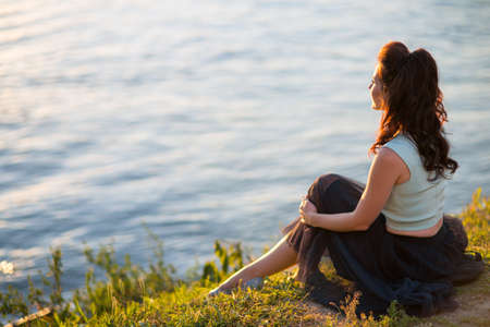 Beautiful young woman sits on the river bankの写真素材