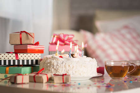 Birthday cake with candles on the table with giftsの写真素材