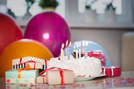 Birthday cake with candles on the table with giftsの写真素材