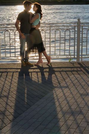 Beautiful young couple sitting on the river bank at sunsetの写真素材