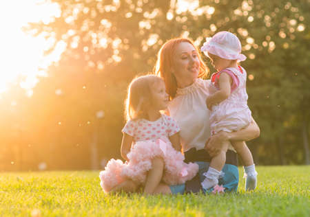 Mom with two daughters sitting in the park on the grassの写真素材