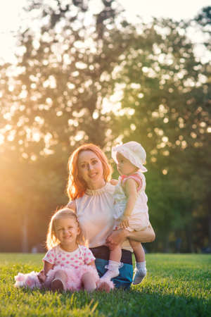 Mom with two daughters sitting in the park on the grassの写真素材