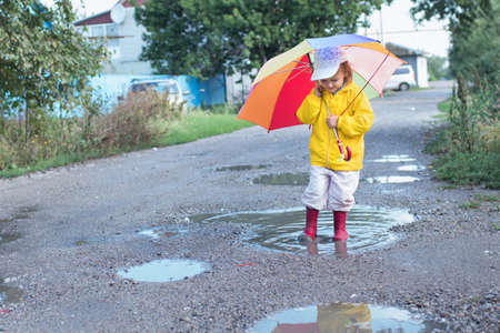 A girl of two years walking in the rain with an umbrellaの写真素材