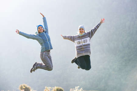 Two young women jumping against the background of mountainsの写真素材