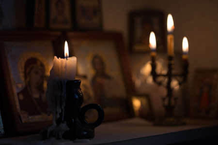 A burning candle against the background of orthodox icons in a dark roomの写真素材