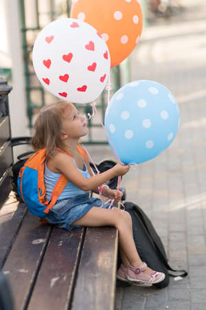 A girl of three years is sitting on a bench with balloonsの写真素材