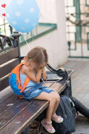 A girl of three years is sitting on a bench with balloonsの写真素材
