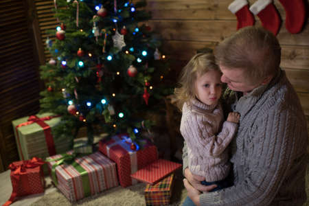 Dad calms the frustrated daughter, near the Christmas tree. distressed child at the feastの写真素材