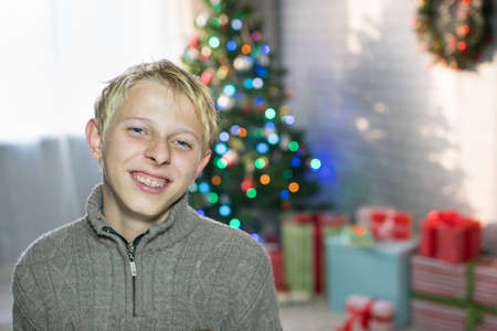 A teenager boy stands in a room with Christmas fir and presentsの写真素材
