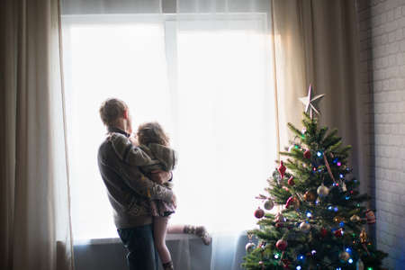 Girl and boy looking at the window in the room with a Christmas treeの写真素材