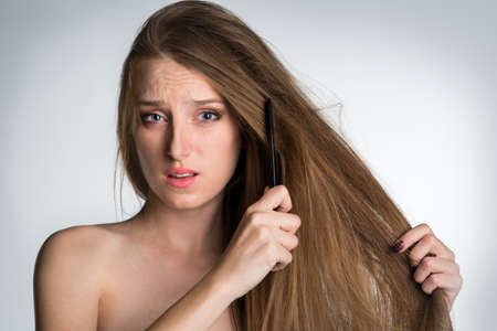A young woman with long hair can not comb her hair, is very confused and brittleの写真素材