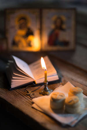 A burning candle against the background of orthodox icons in a dark room