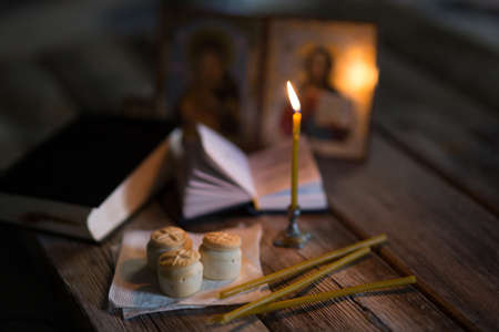 A burning candle against the background of orthodox icons in a dark room
