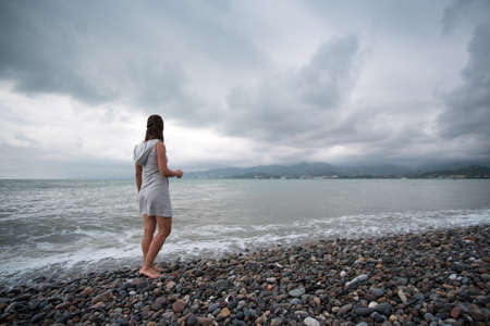 Beautiful young woman admires the sea in cloudy weather.