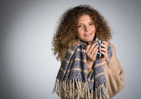 Young woman with curly hair, A woman in a scarf is frozen drinking hot teaの写真素材