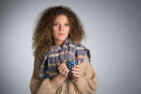 Young woman with curly hair, A woman in a scarf is frozen drinking hot teaの写真素材