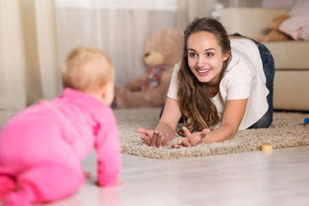 A young mother plays with a baby. A woman plays with a baby eight months of age