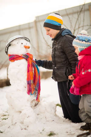 Children mold Snowman with a carrot in the yard winter, Boy and girl play with snowの写真素材