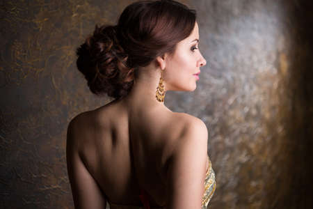 Young beautiful elegant woman in evening gold dress with beautiful hairdoの写真素材